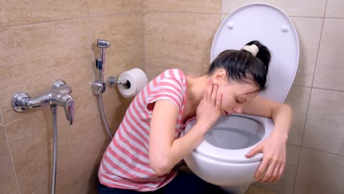 年轻的孕妇在家里坐在地板上的厕所里呕吐。