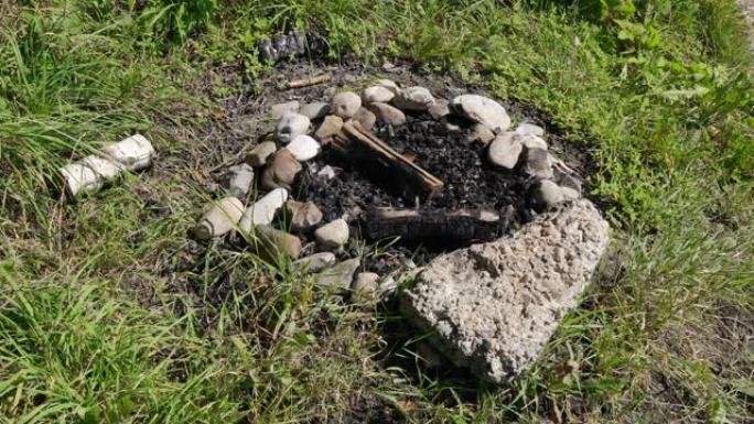 在刮风的天气中，白天在绿色的草地上熄灭了烧焦的烧焦木头的石头壁炉，没有人