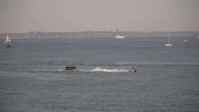 在炎热的夏日午后，摩托艇在度假小镇的海岸上拖曳着一个充气平台。海湾水上和海上运输的极端娱乐。