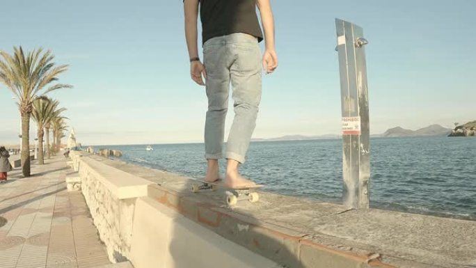 穿着牛仔裤和黑色短袖t恤的年轻人在大海为背景的码头上赤脚滑冰