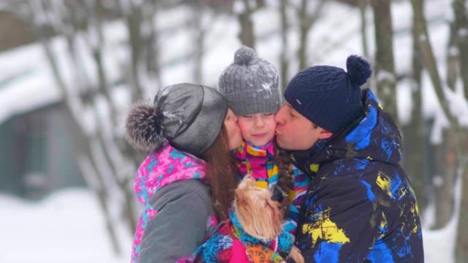 细心的父母在白雪皑皑的森林里用小狗亲吻女孩