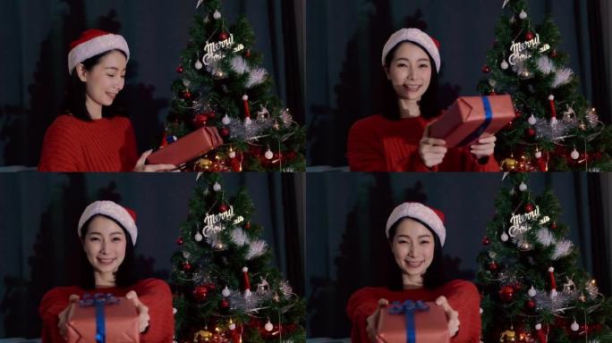 戴红帽子的亚洲女人送礼盒，在客厅说 “新年快乐” 和 “圣诞节”