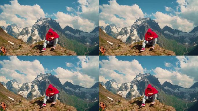 男子游客坐在山上的岩石上，智能手机。男性旅行者在山区晴天使用手机对抗多云的天空