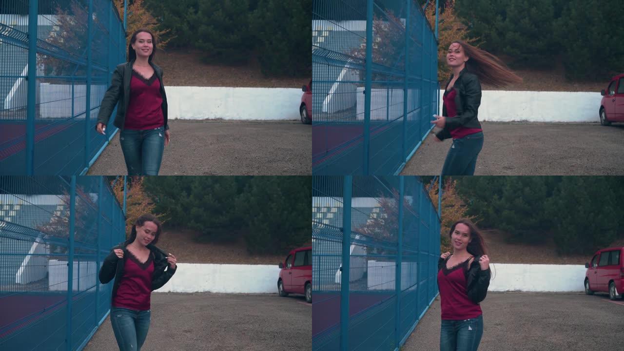 一个美丽而热情的女孩沿着运动场的铁栅栏行走。年轻女子快乐地迈步。