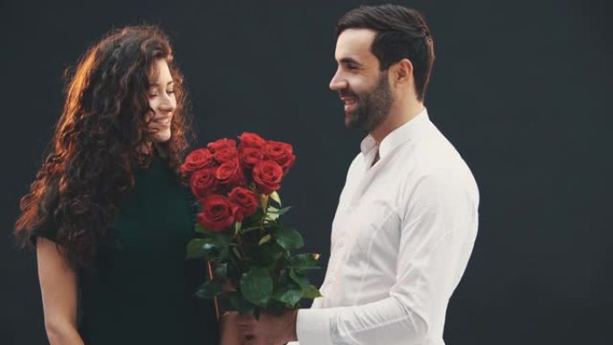 浪漫的年轻人给女友一束红玫瑰。他们躲在花后面接吻。