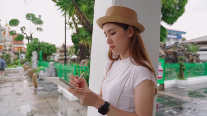 时髦的伦斯特女孩站在笔记本上涂鸦，游览黎明神庙。泰国的热门地点。