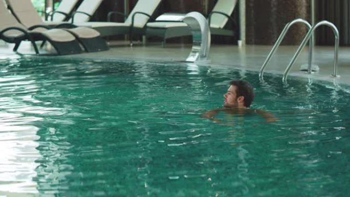 快乐的人在度假的现代酒店游泳。英俊的男人在游泳池洗澡。