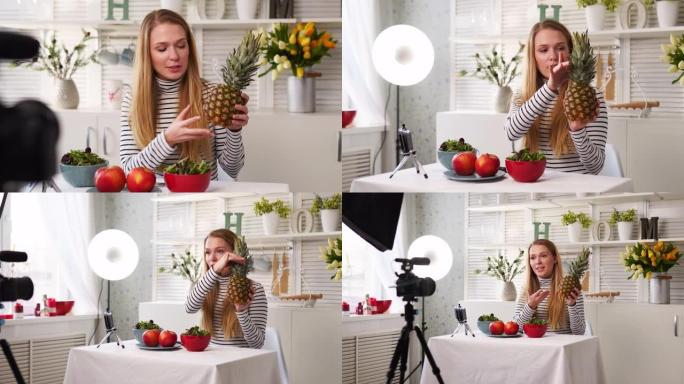 食物博主在厨房工作室烹饪新鲜的水果素食沙拉，在视频频道的相机上拍摄教程。女性影响者手持苹果、菠萝，谈
