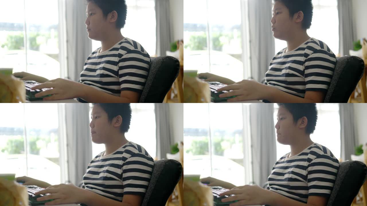 快乐的亚洲青春期男孩使用电脑做家庭作业或玩网络游戏，生活方式概念。
