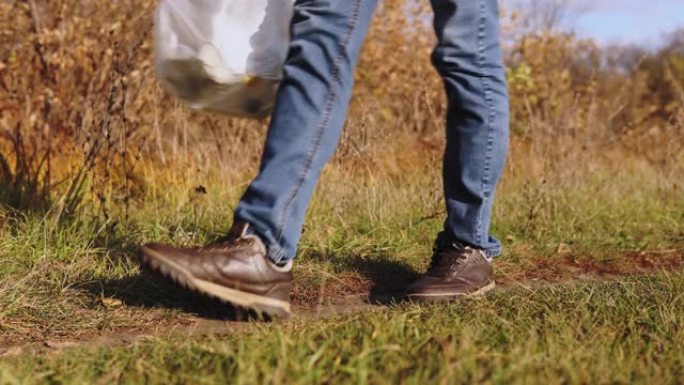 生态概念塑料污染。一个穿着蓝色牛仔裤的不负责任的男人在自然界中扔了装有塑料瓶的袋子。