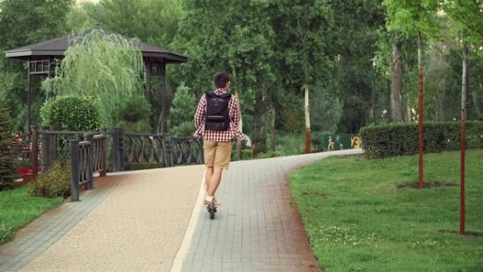 生态主题，新型个性化智能交通电动推代步车。高加索人沿着自行车道骑着一辆环保踏板车穿过城市公园。男性骑