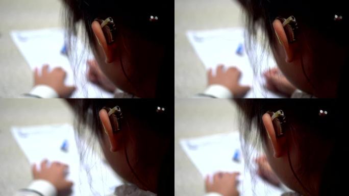 听力损失的女孩在做作业。主题在右边。穿着条纹衣服。右手拿着铅笔。