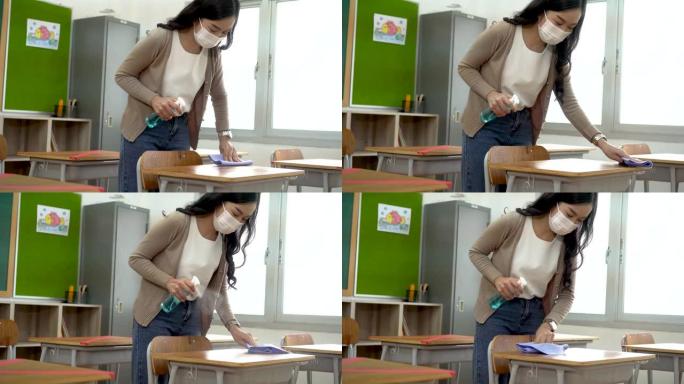 年轻女教师使用酒精喷雾器给教室里的学生课桌消毒。亚洲妇女戴着口罩，用杀菌剂清洁桌子。学校在隔离和封锁