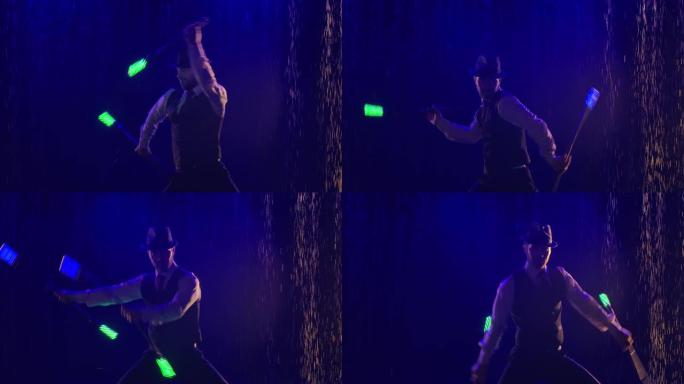 一个时髦的男人在蓝光照亮的水滴背景下表演的灯光表演。艺术家在晚上被荧光棒剪影。慢动作。特写