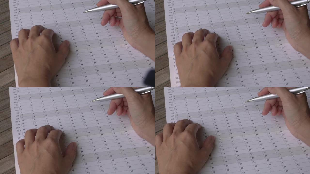 女人用手指，用笔穿过年度日历计划器。特写视图