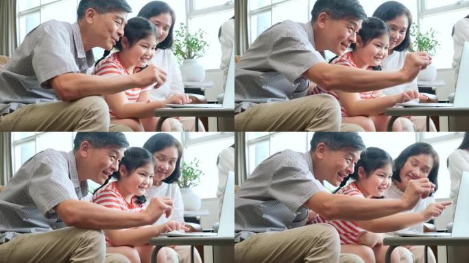 爷爷奶奶教小儿子孙女用笔记本电脑坐在沙发上，幸福的关系结合一代亚洲家庭花时间在网上玩笔记本电脑在家里