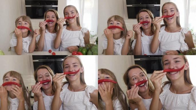 两个穿着白色衣服的姐妹和他们的母亲在厨房里玩辣椒。女孩用红辣椒做小胡子，看着相机玩得开心