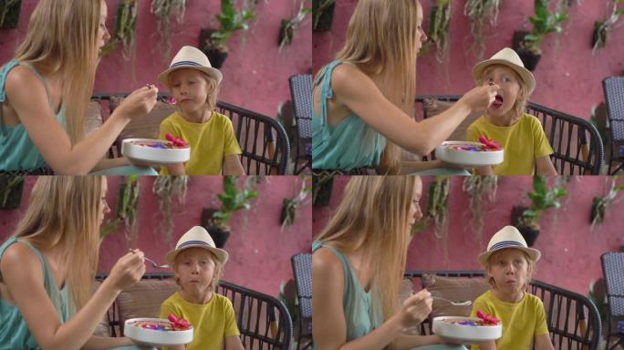 年轻女子和她的小儿子坐在一个美丽的咖啡馆里，在碗里享受五颜六色的格兰诺拉麦片冰沙。健康饮食理念。慢动