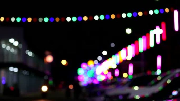 夜市集市上模糊霓虹灯和剪影车的多彩