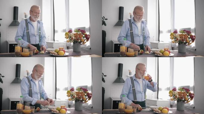 戴眼镜胡子的老peppy男人适当营养的爱好者准备健康的水果沙拉提饮料维生素汁，同时站在餐桌上美丽的厨
