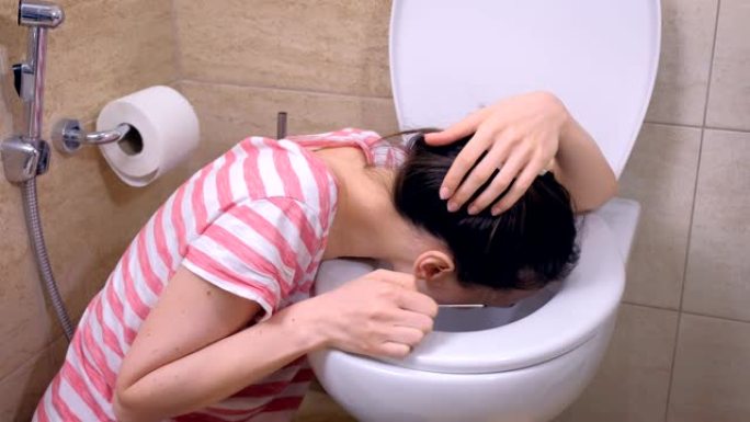 晨吐。年轻的孕妇在家里坐在地板上的厕所里呕吐。