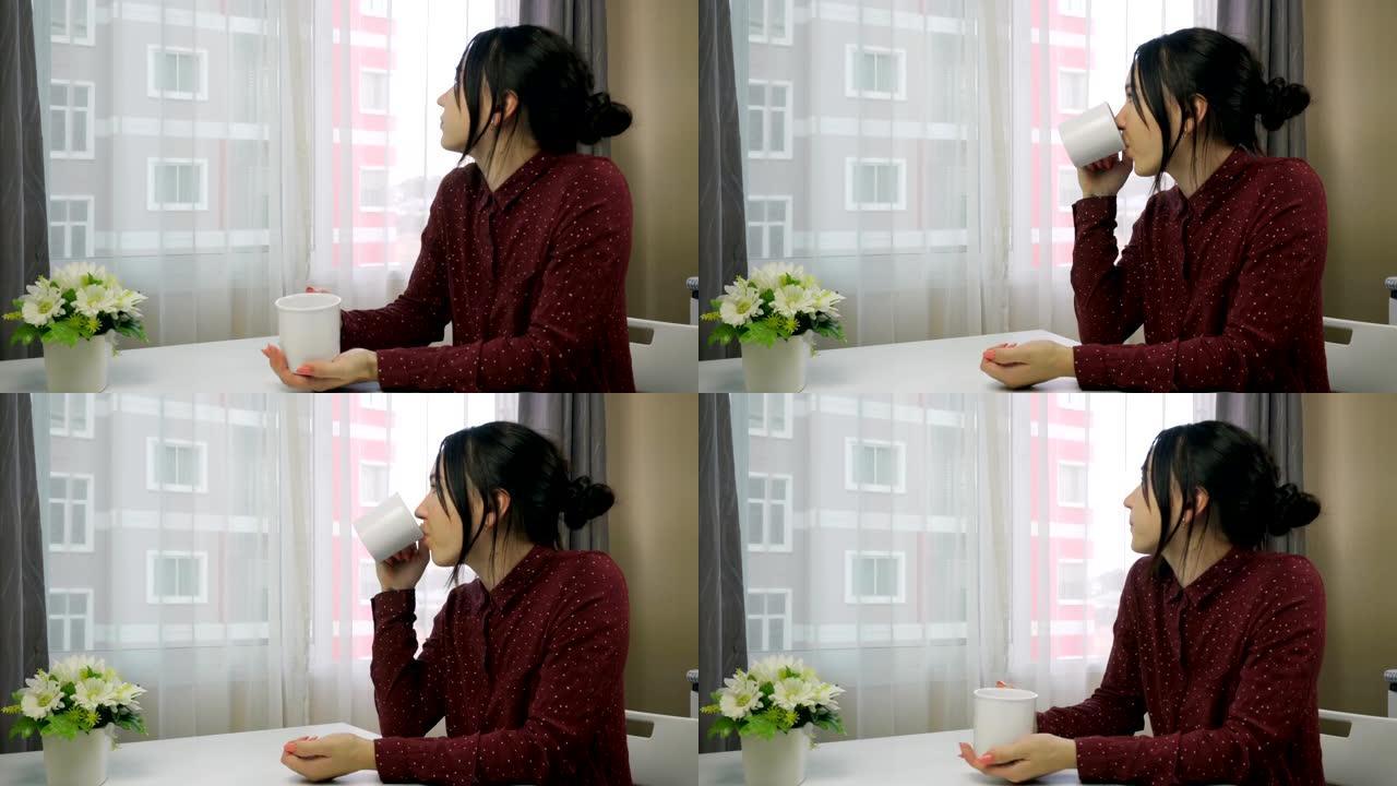 一名年轻女子站在窗边喝咖啡。