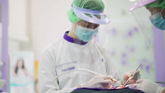 亚洲男性牙医用保护性面罩和塑料护罩为他的病人工作