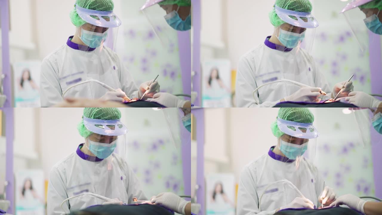 亚洲男性牙医用保护性面罩和塑料护罩为他的病人工作