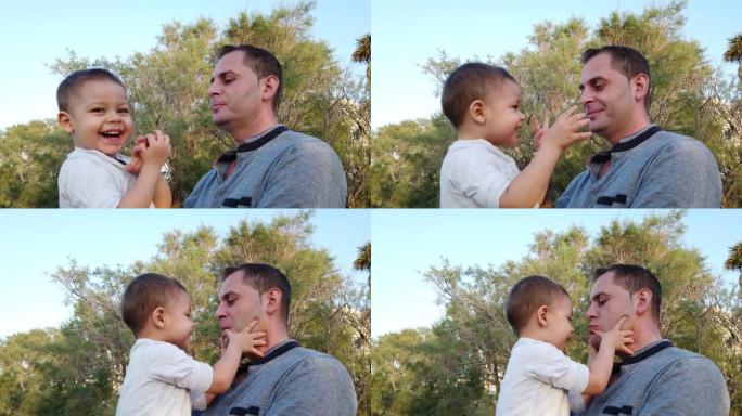 年轻的高加索父亲抱着儿子蹒跚学步。婴儿抚摸父亲的脸，两人都做有趣的脸