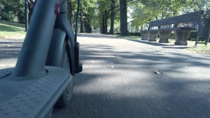 夏天乘坐电动滑板车穿过公园。踏板车的前轮在前台。低角度视图。