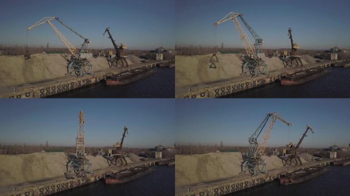 码头附近岸上的大型港口起重机将河沙驳船卸载到一个大堆上。运输散装货物的火车。货港的工作。航空摄影无人