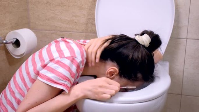 疼痛的年轻孕妇正在坐在家里地板上的厕所呕吐。