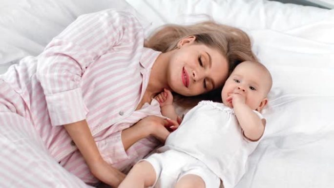 放松的女人和小婴儿微笑着躺在白色床上。4k龙红相机