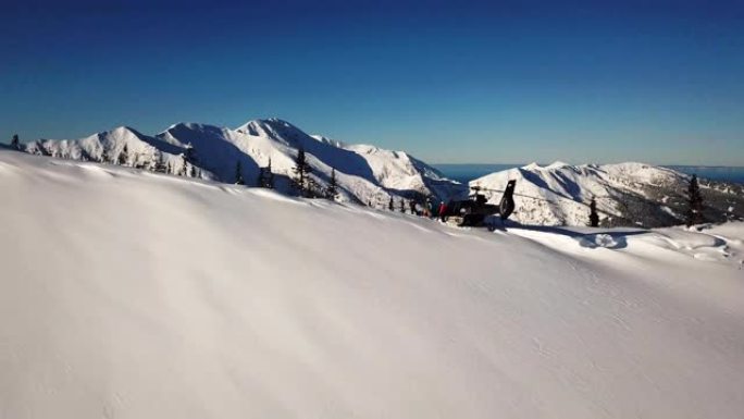 Actionsportlers被一架直升机降落在山顶。蓝蓝的天空中艳阳高照。背景中有一条山脉被雪覆盖