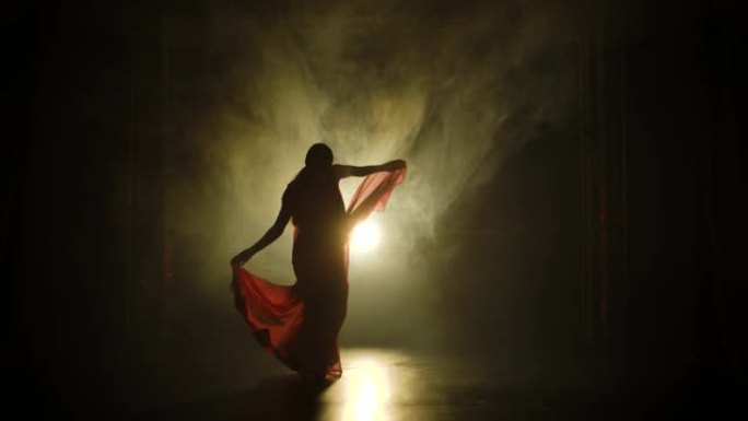 剪影一个穿着红色纱丽的年轻女孩舞者。印度民间舞蹈。在黑暗的工作室里拍摄，有烟雾和霓虹灯。慢动作