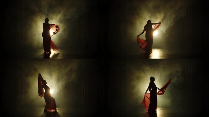 剪影一个穿着红色纱丽的年轻女孩舞者。印度民间舞蹈。在黑暗的工作室里拍摄，有烟雾和霓虹灯。慢动作