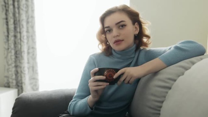 年轻漂亮的女人坐在舒适的沙发上喝茶