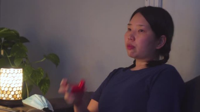年轻的亚洲妇女在家里使用吸入器看电视