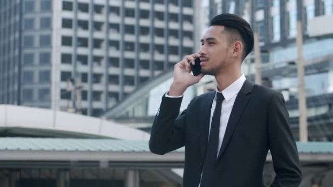 中枪。年轻的亚洲商人在这座城市的建筑背景下与智能手机上的客户交谈。