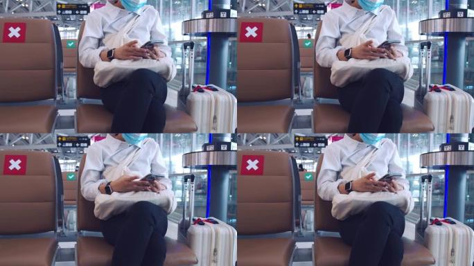 女商人戴着外科口罩保护，并在机场候机楼坐在椅子上使用智能手机检查社交媒体供稿，并在新型冠状病毒肺炎大