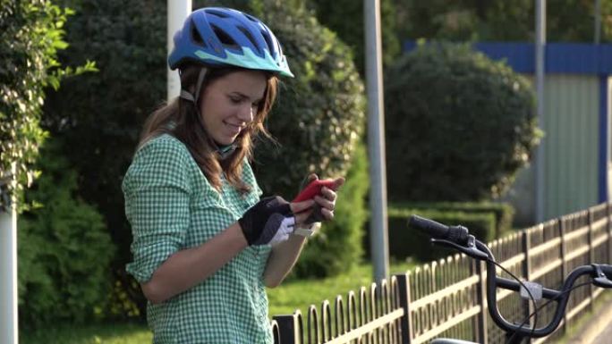 年轻的高加索女学生使用手持电话触摸屏。在阳光明媚的天气里，一名妇女穿着头盔和衬衫站在人行道上的出租城