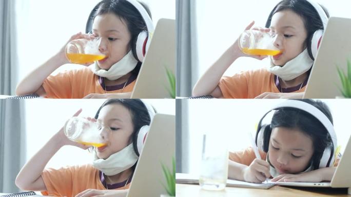 亚洲女孩喝一杯橙汁，同时学习电子学习从家里新型冠状病毒肺炎，生活方式的概念。