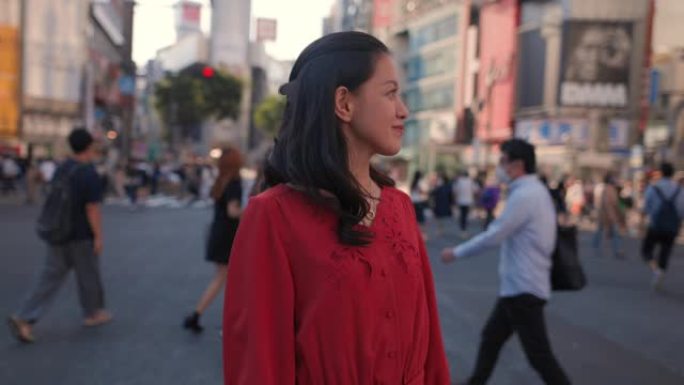 身穿红色连衣裙的年轻女子站在涩谷十字路口，望着远处