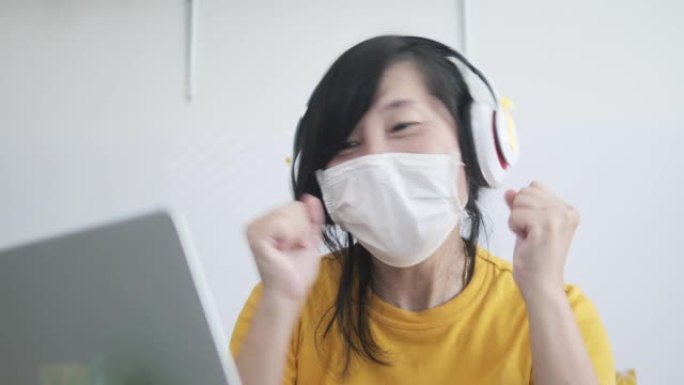 快乐的亚洲女人在熨衣板上使用笔记本电脑或在新型冠状病毒肺炎期间在家工作。