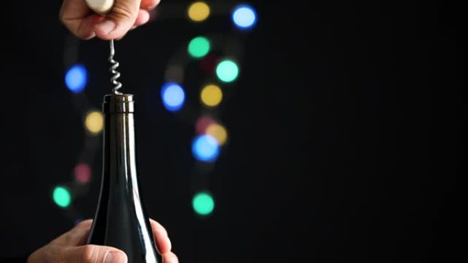 男子在黑暗的节日背景上打开一个红酒瓶，并带有彩色的bokeh
