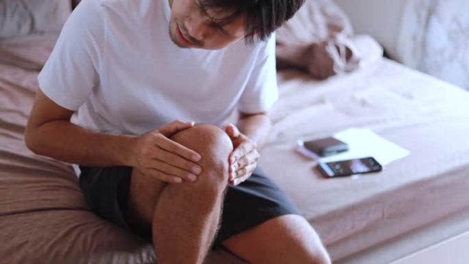 年轻的亚洲男子膝盖按摩在卧室