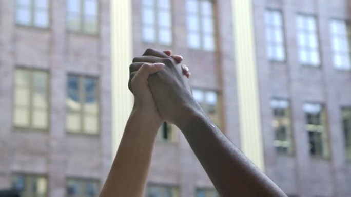 反种族主义象征。黑色和白色的双手握紧拳头，以抗议城市街道的背景。革命概念。特写。慢动作