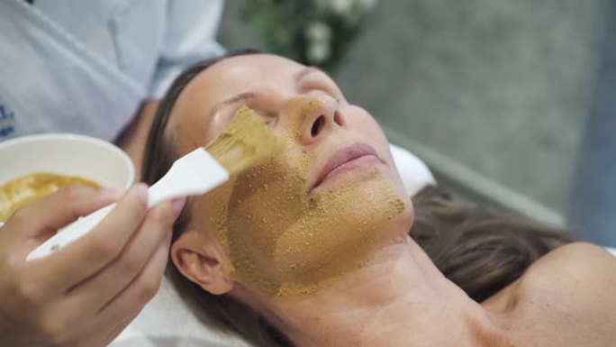 专家在女性脸上涂抹脱皮面霜面膜