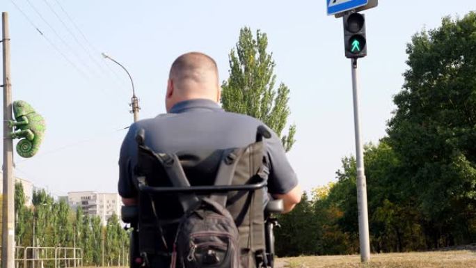轮椅男子。残疾人。后视图。坐轮椅的年轻残疾人在人行横道过马路。绿色交通灯在背景上