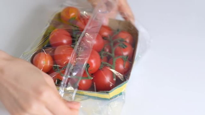 女人用食物薄膜在白色桌子上储存食物。一次性塑料包装的樱桃番茄。慢动作视频。特写